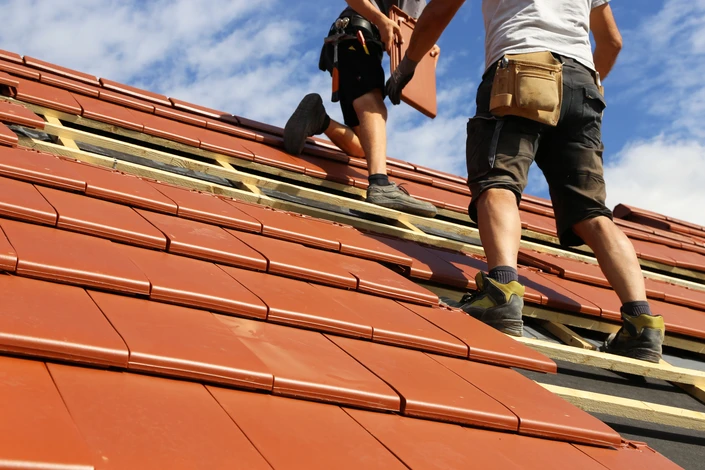 Deux couvreurs travaillant sur une toiture en pente, installant des tuiles terre cuite rouge