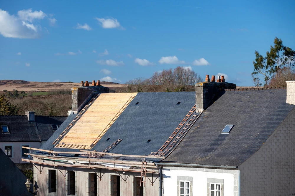 Chantier de construction extérieur avec ouvrier en gilet haute visibilité orange travaillant sur charpente bois