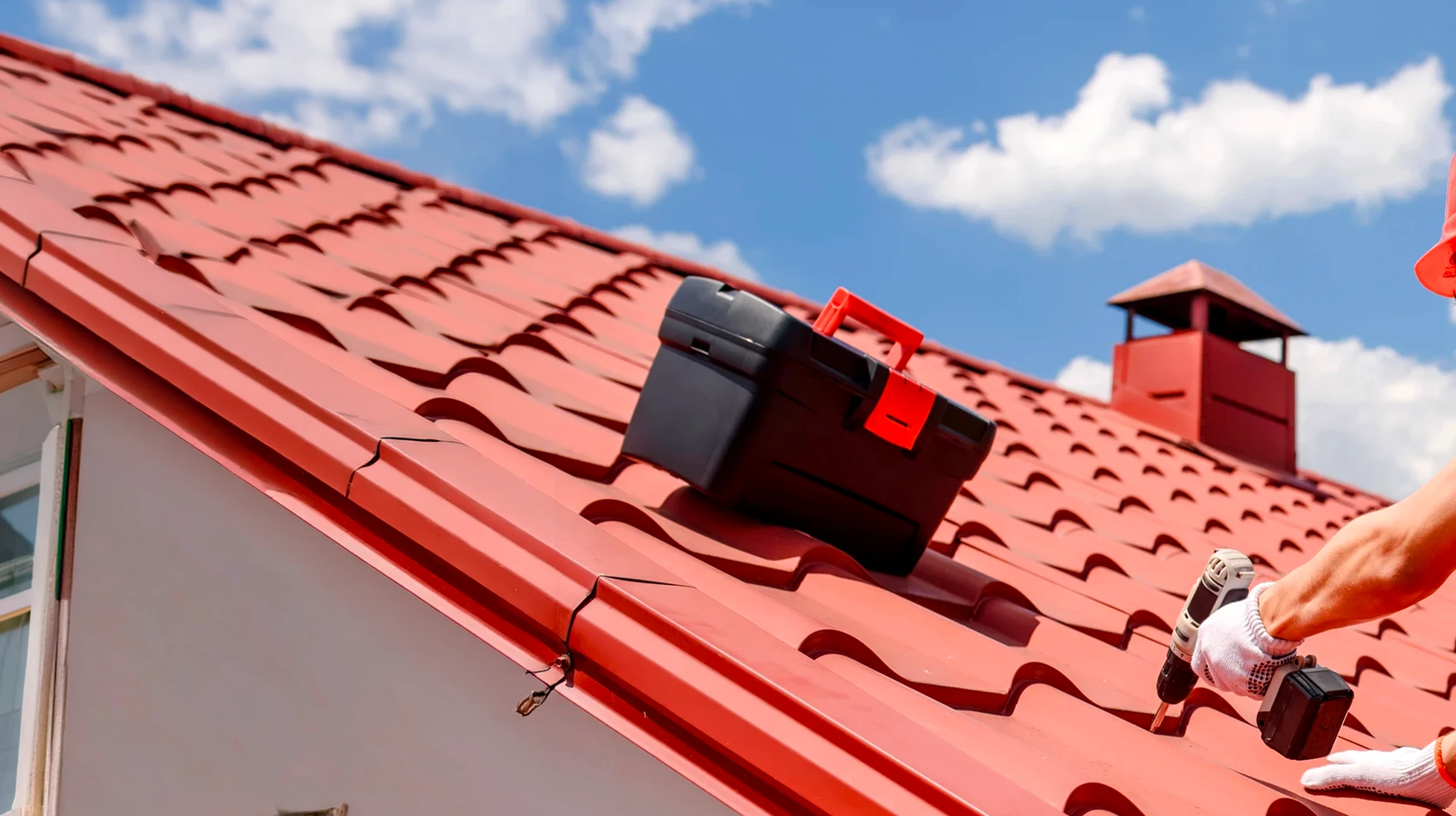Ouvrier en combinaison rouge et casque de sécurité effectuant des travaux de maintenance sur toiture en tuiles terre cuite