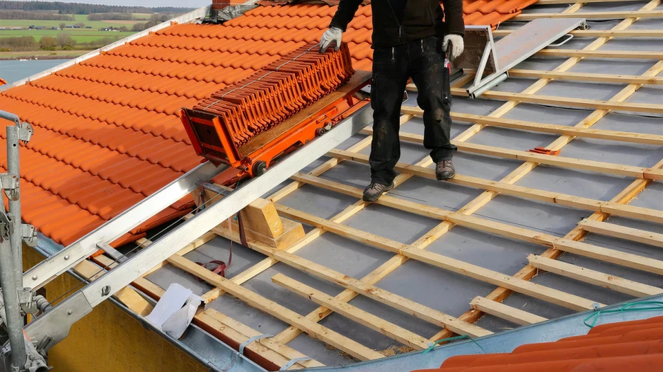 Chantier de couverture en extérieur avec ouvrier couvreur installant des tuiles terre cuite sur toiture résidentielle